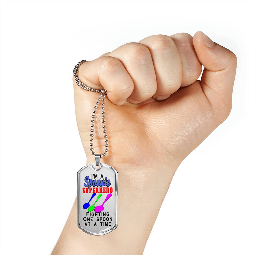 A clenched fist holds a dogtag which says, "I'm a Spoonie Superhero Fighting One Spoon At A Time" Necklace