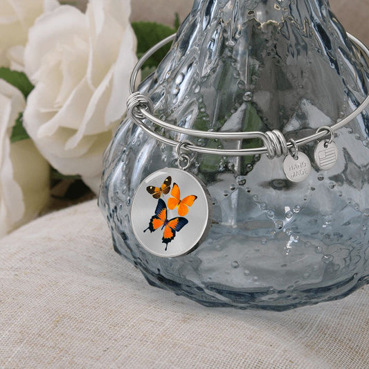 Orange Butterfly Charm on a wire frame Bangle bracelet sits over a crystal vase next to white roses