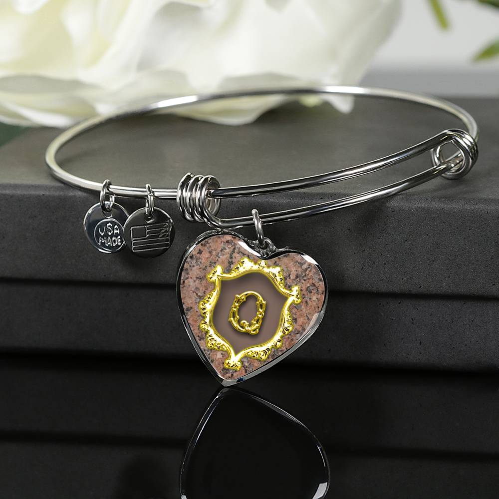 Heart Pendant Q Monogram Alphabet Initial Bangle draped over the giftbox on a glass tabletop